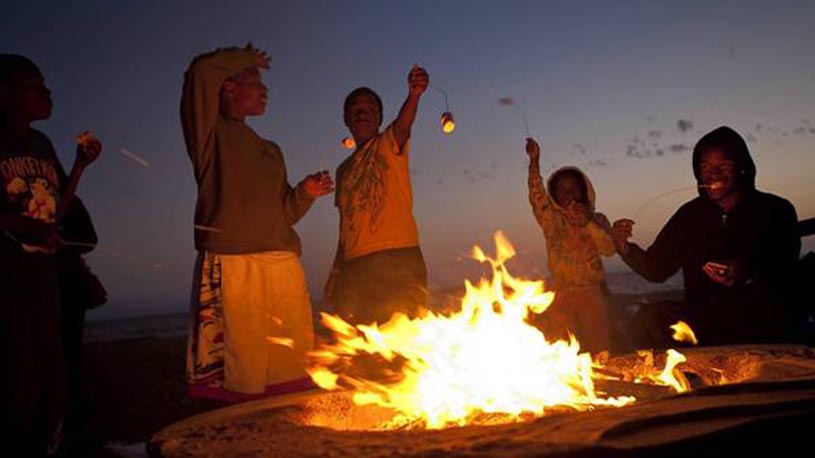 Schaben, Allen J. –– B582268822Z.1 PLAYA DEL REY, CA – AUGUST 4, 2012: Members of the Sasser–Williams family, of Los Angeles, roast marshmallows as they gather around a bon fire in a fire pit at sunset at Dockweiler State Beach in Playa del Rey. Dockweiler State Beach is also the only piece of shoreline in Los Angeles County where people are allowed at night. (Allen J. Schaben / Los Angeles Times)